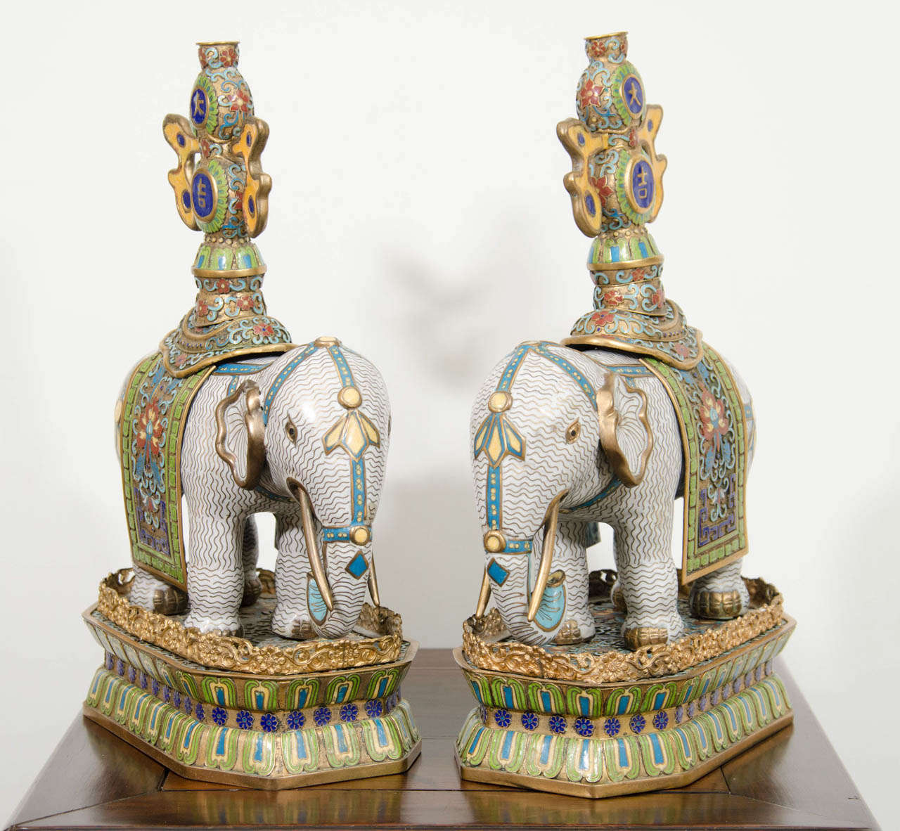 A pair of Chinese late Qing Dynasty gilt bronze elephants in colored cloisonne and champleve enamel and decorated with double gourd urns on their saddle carpets.  Each urn is marked, 