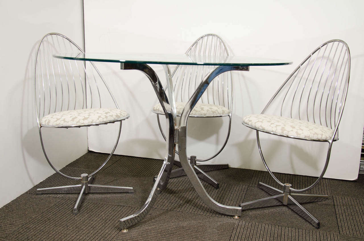 A vintage chrome and circular glass table with a set of three wire form swivel chrome chairs attributed to Dahlens Dalum.  The removable seat cushions have been newly reupholstered.  The chairs vary slightly at the base and one chair is missing its