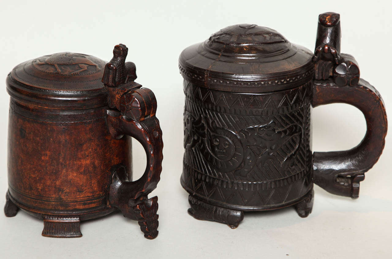 A good collection of five Norwegian tankards, including three birch burl peg tankards with lion handles, one rustic willow banded green painted tankard with pouring spout and an unusual willow banded tankard in salmon and black paint having a carved