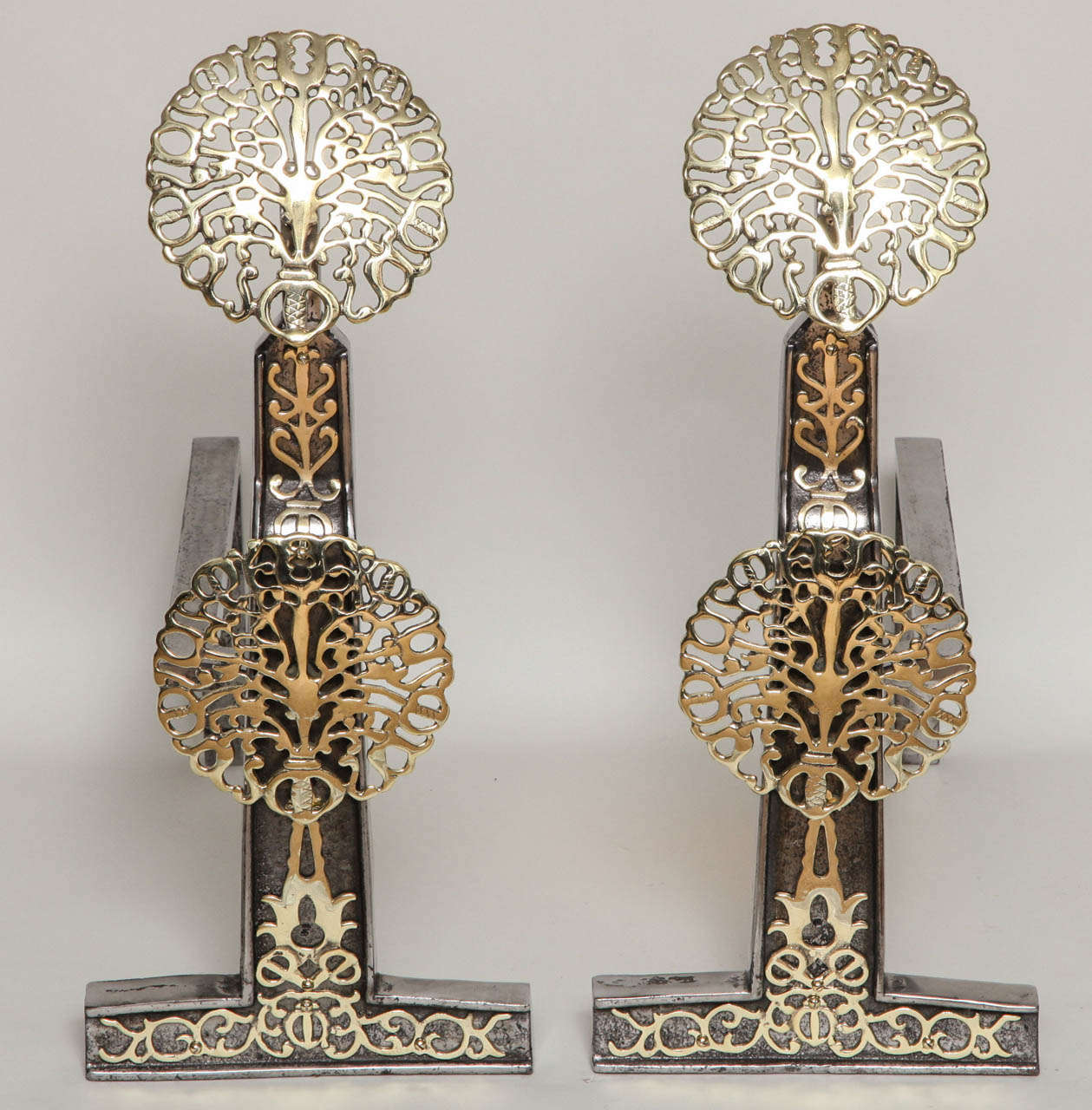 An exceptional pair of English andirons, possibly by Earnest Gimson having double blossom brass bosses applied to and iron backing, the shaft having similar applied pierced decoration, all of very fine quality.  See the Cheltenham Museum collection