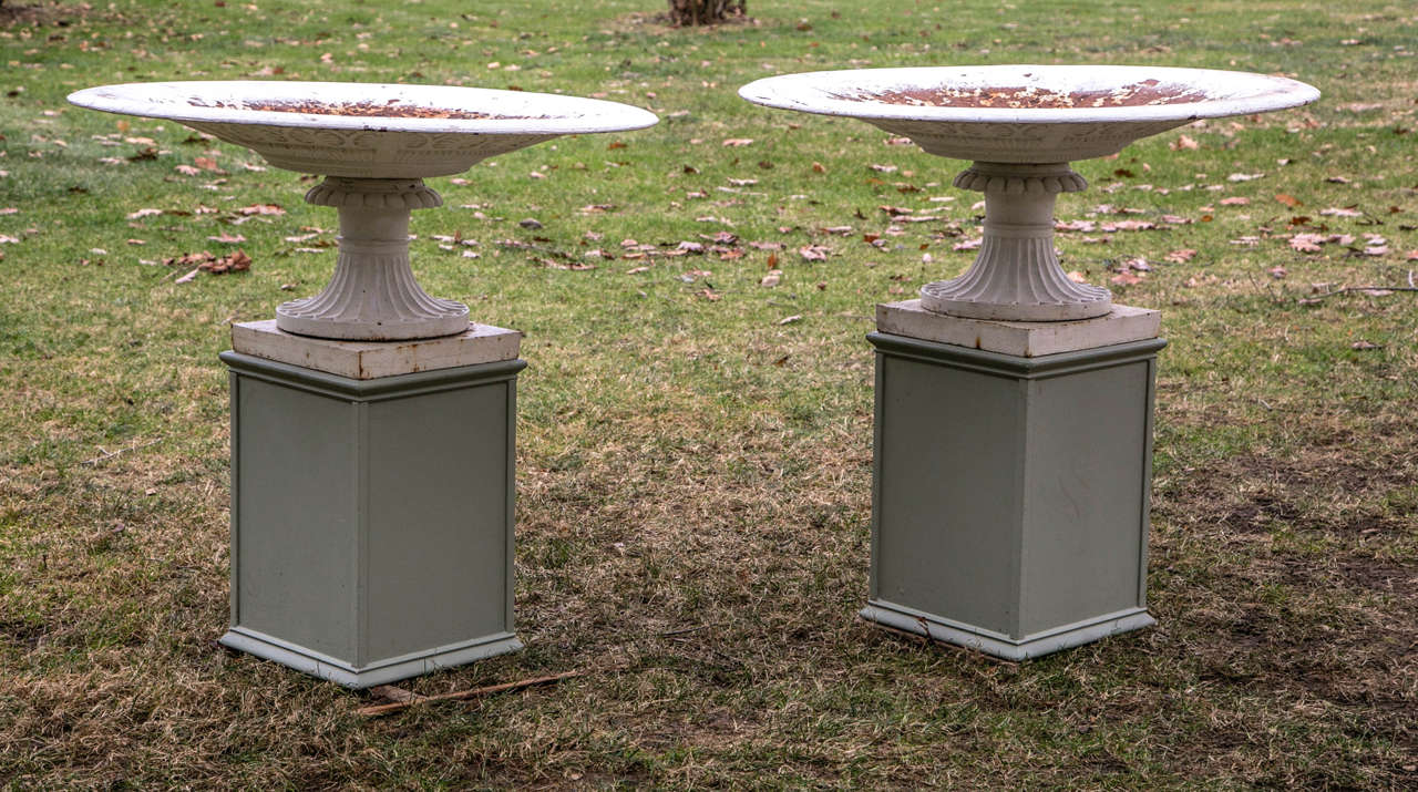 A pair of large shallow cast-iron tazza form urns, each with anthemion motif on underside of bowl, on fluted socles and integral square bases.  Wood pedestals not included.