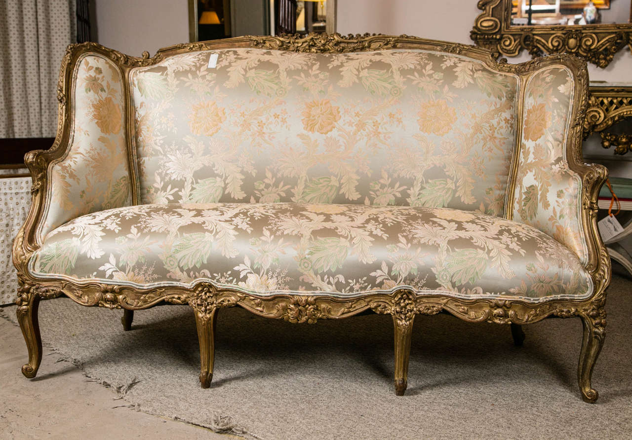 This quality Louis XV Style Carved French Sofa by Jansen will light up any room setting.  This wonderfully carved sofa / large canapé is carved with all around solid wood leafs, vines and flowers in a gilt finish. The fine silk upholstery in good