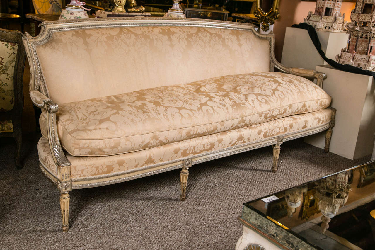 A finely upholstered Louis XVI style sofa by Maison Jansen. The wonderfully cream and silver gilt decorated sofa having the finest quality carvings. Perched on carved tapering legs and having a carved and silver gilt paint decorated apron leading to