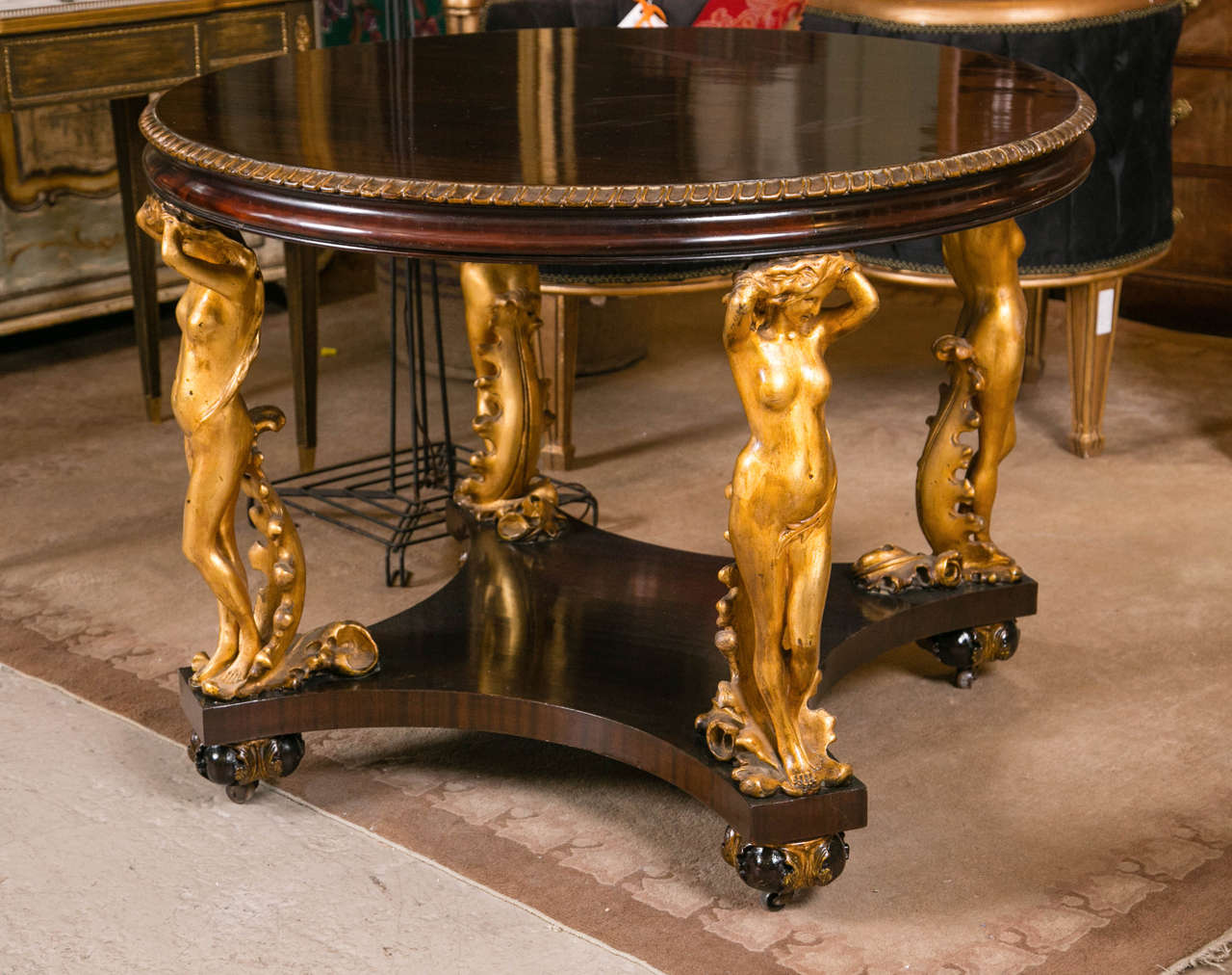 A Antique Carved Figural Center Table. This antique center table is a one of a kind piece having finely carved feet with rollers under a gilt leaf carved bun supporting a center lower shelf having four finely chiseled naked maidens holding up a