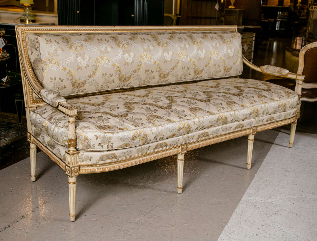 Louis XVI style sofa by Maison Jansen. Wonderfully upholstered in silk and linen. The parcel paint decorated and gilt gold sofa is constructed by hand. The tapering legs support a carved apron leading to a down cushion flanked by wood armrests and a