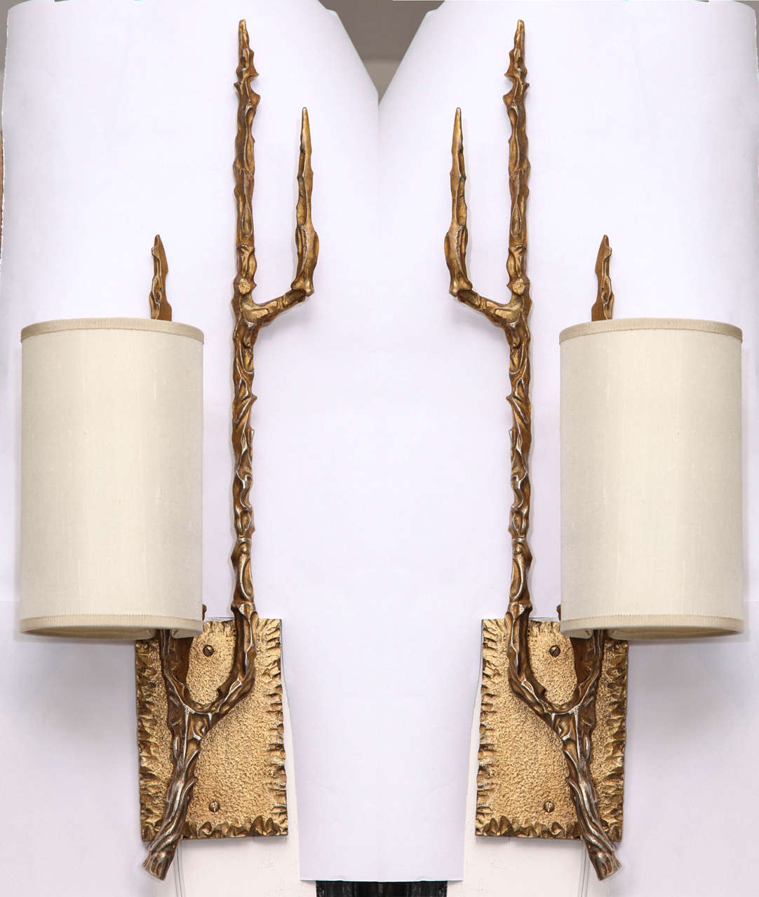 A pair of 1960s Brutalist style sculptural sconces, crafted of patinated bronze in the form of elongated branches, affixed to textured back-plates.