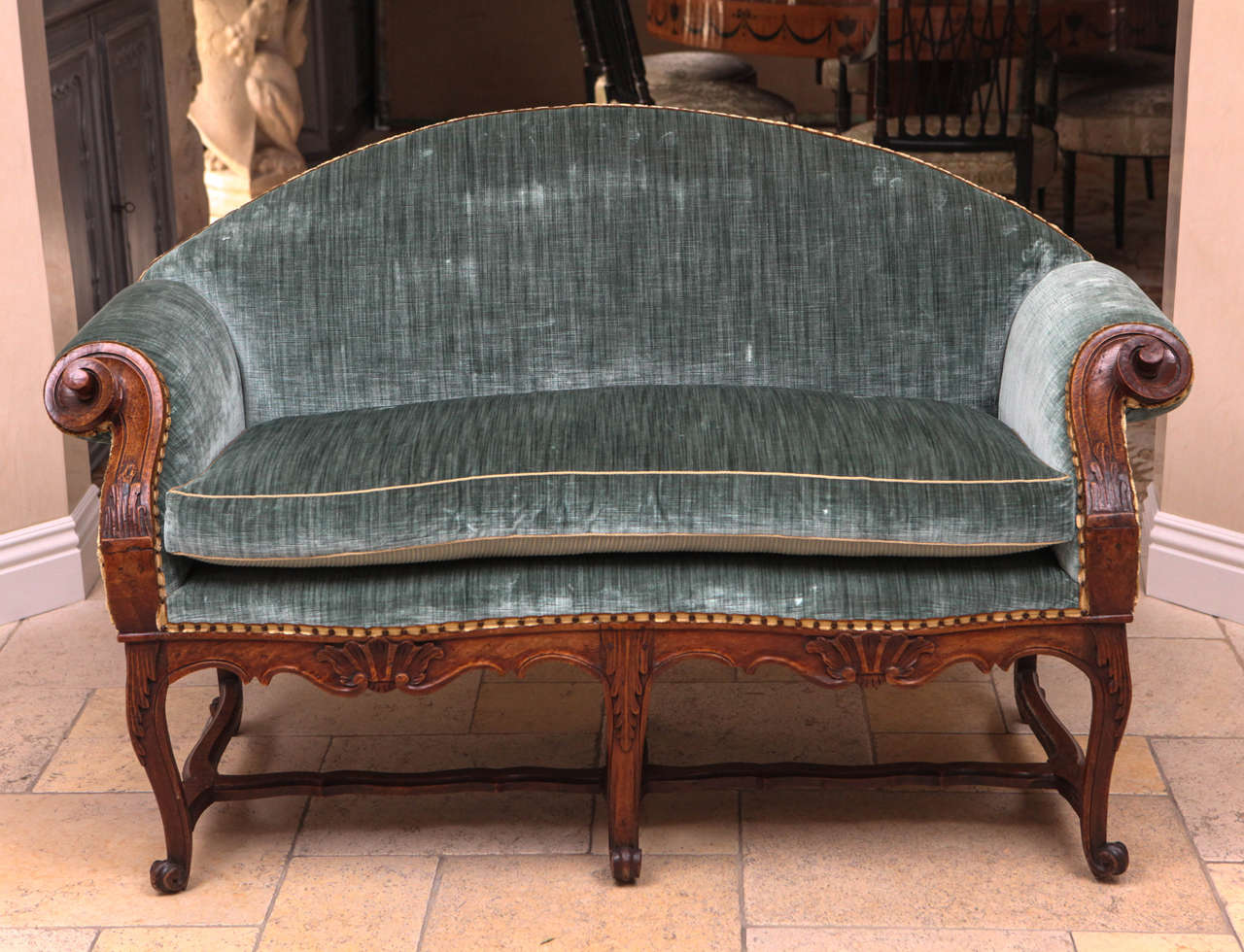 18th century French Regence walnut settee finely carved with scrolled arms. The settee is covered in silk velvet fabric.