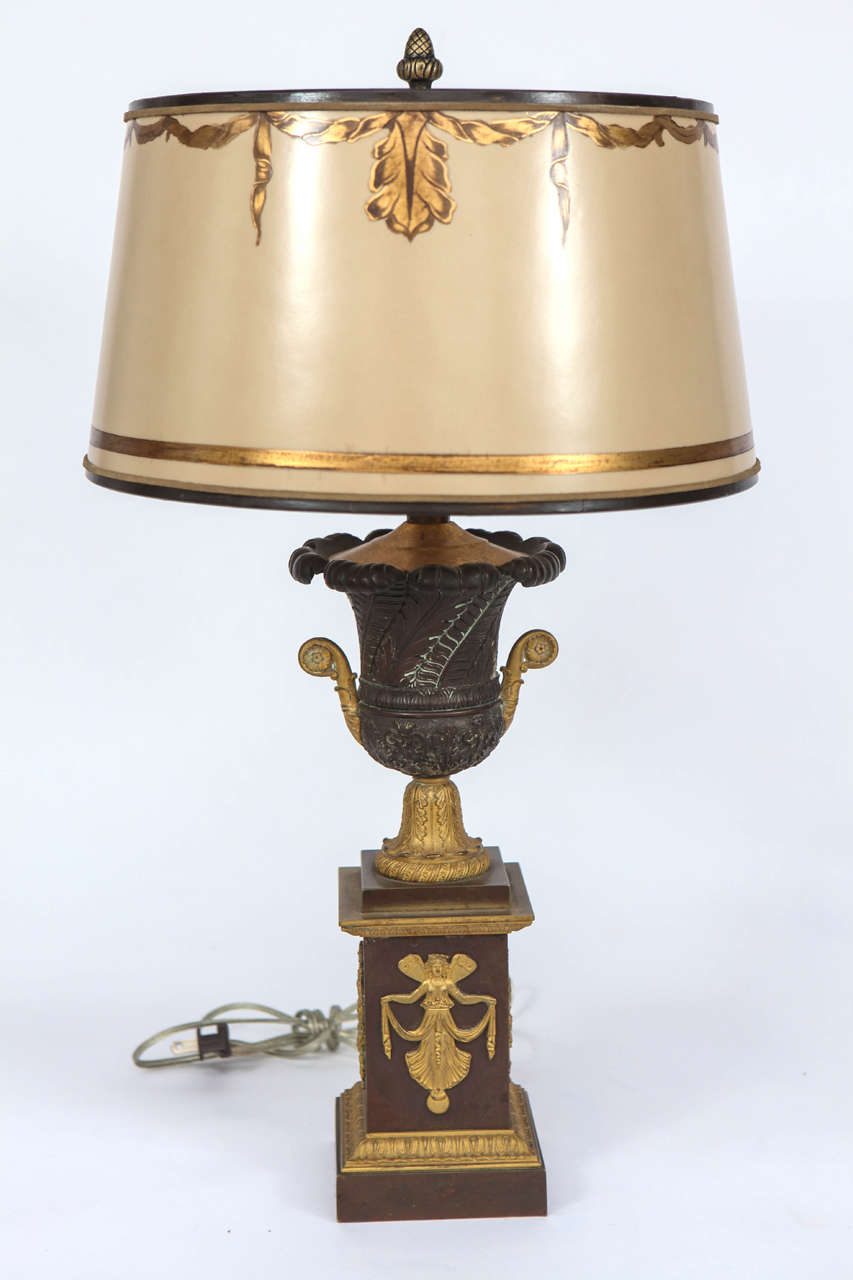 Pair of 19th century French Empire bronze urns converted to lamps. The base measurement is 4 inches. The shades are included and are handmade of parchment paper. They are hand gilded and decorated. The lamps have been newly wired.