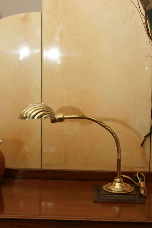 A turn-of-the-century brass gooseneck lamp with a brass shell mounted on a wooden base.