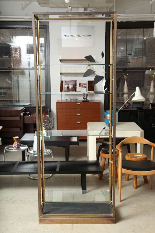 Jacques Adnet attributed etagere with four adjustable glass shelves and a brass/wood base. This piece was originally a vitrine with locking side glass doors. 