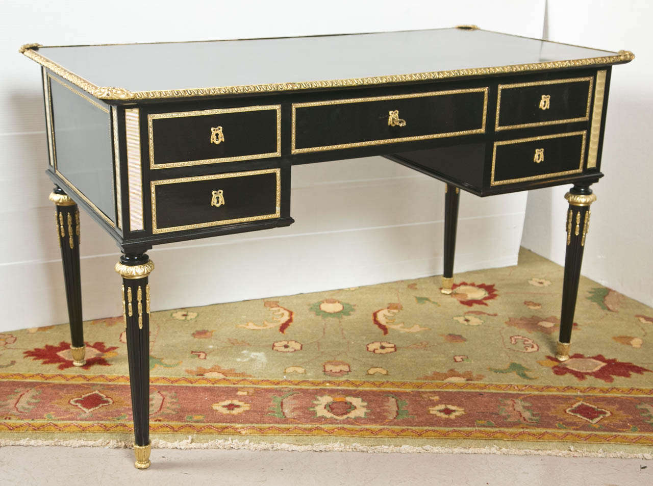 French ebonized bureau plat in the taste of Louis XVI, circa 1940's, the top having bronze banding, over a central drawer flanked by two sets of drawers each side, bronze banding throughout, raised on fluted tapering legs ending in bronze caps. By