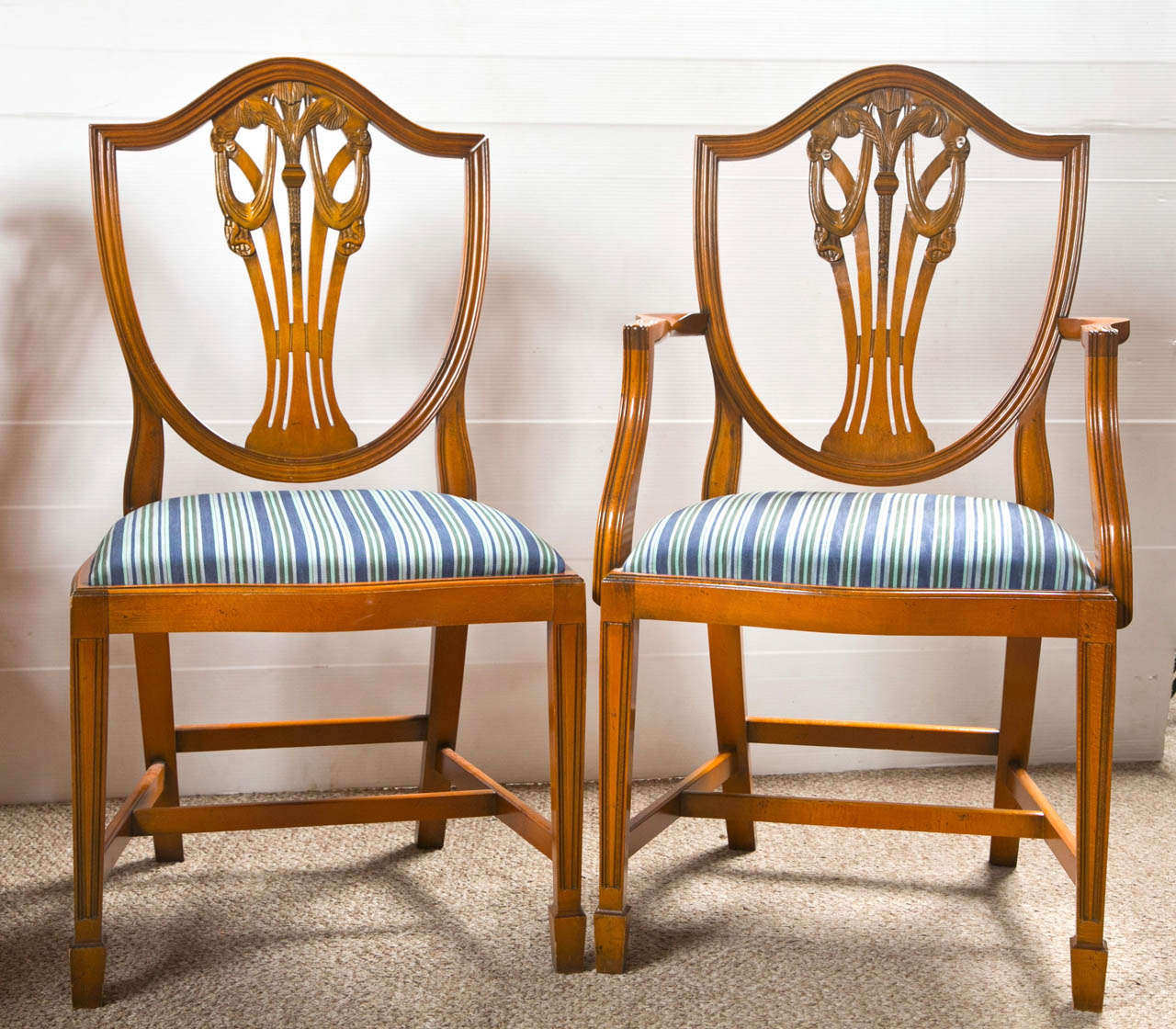 Set of 12 walnut dining chairs in the Sheraton style, 2 armchairs and 10 side chairs, possibly from the 1940s, each having a shield back decorated with plume and drapery motif splat, padded seat, raised on squared legs joint by H stretcher, ending