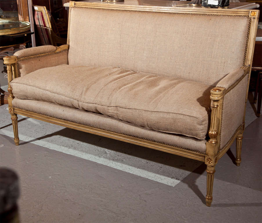 French Louis XVI style canape or settee, overall distress-painted and parcel-gilt, upholstered in burlap, padded back and arm rests, cushioned seat, raised on fluted legs. By Maison Jansen.