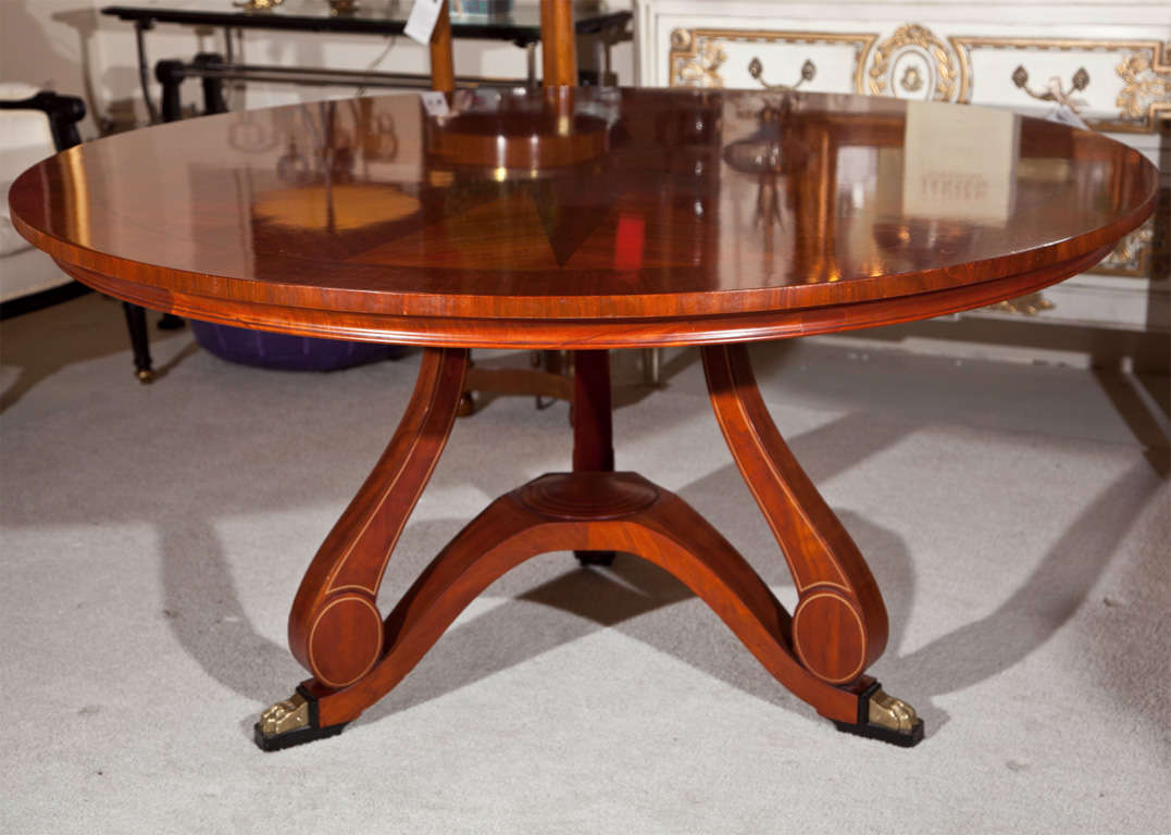 A handsome mahogany round dining table by John Widdicomb, circa 1960s, the molded cross-banded top depicting a starburst pattern, supported by a single pedestal with three scrolled legs, ending in bronze claw feet.