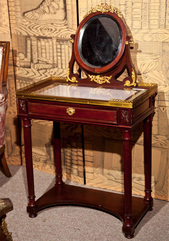 Spectacular French Louis XIV style mahogany vanity table, possibly first quarter of 20th century, the looking glass with parcel-gilt carved crest sets on a rectangular glass top with bronze gallery, over a frieze fitted with a single drawer, raised