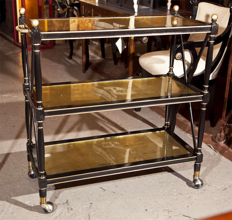  French Directoire style ebonized three-tier serving cart, circa 1940s, overall ebonized with parcel-gilt decoration. Each shelf has antiqued gilt glass top, the top shelf with bronze twisted handles on the side and four matching bronze finials,