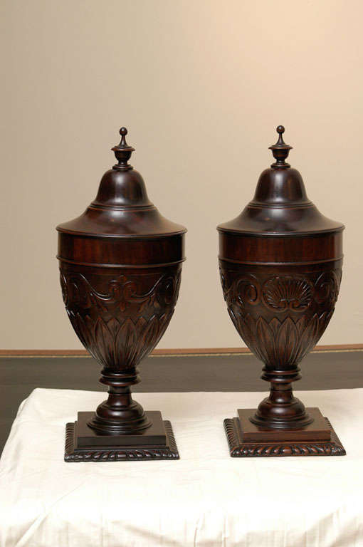 A fine pair of carved Neoclassical Style mahogany knife urns,  Each with a domed top with a turned finial over urn bases fitted with cutlery dividers. The urns are decorated with acanthus leaf and shell carving in relief.<br />
<br />
<br />
View