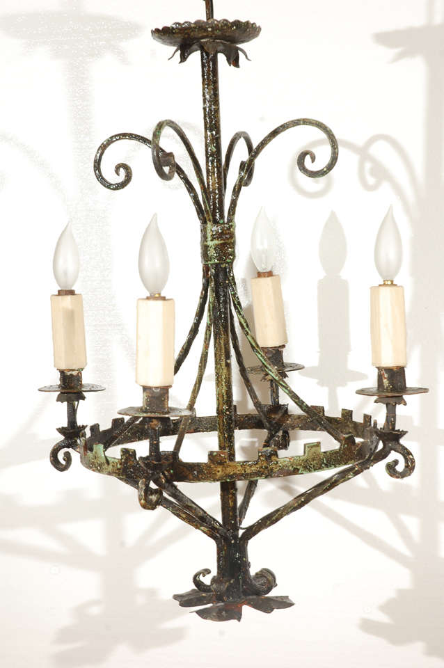 Hand wrought iron four light chandelier with scrolled accents at top, and bottom. Cut center ring holds four lights with hand trimmed candle covers. Very rustic, heavily patinated piece.  Electric in working order. 
25