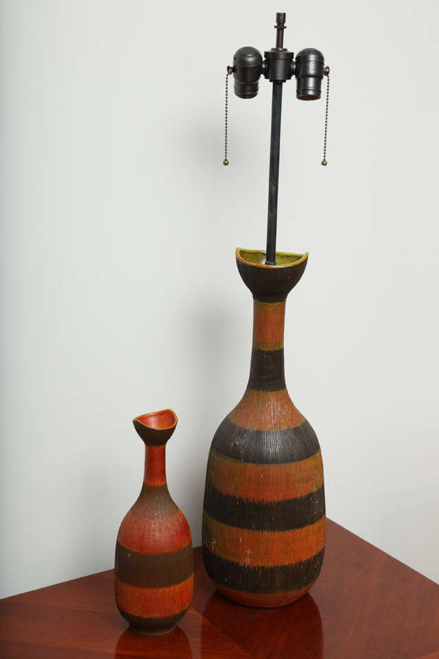 A two-piece set that includes a striped ceramic table lamp and matching smaller vase.  By Raymor.  Italy, circa 1960.  Signed on base.  Features a textured surface with wide orange/red and brown stripes.   Includes off-white drum
