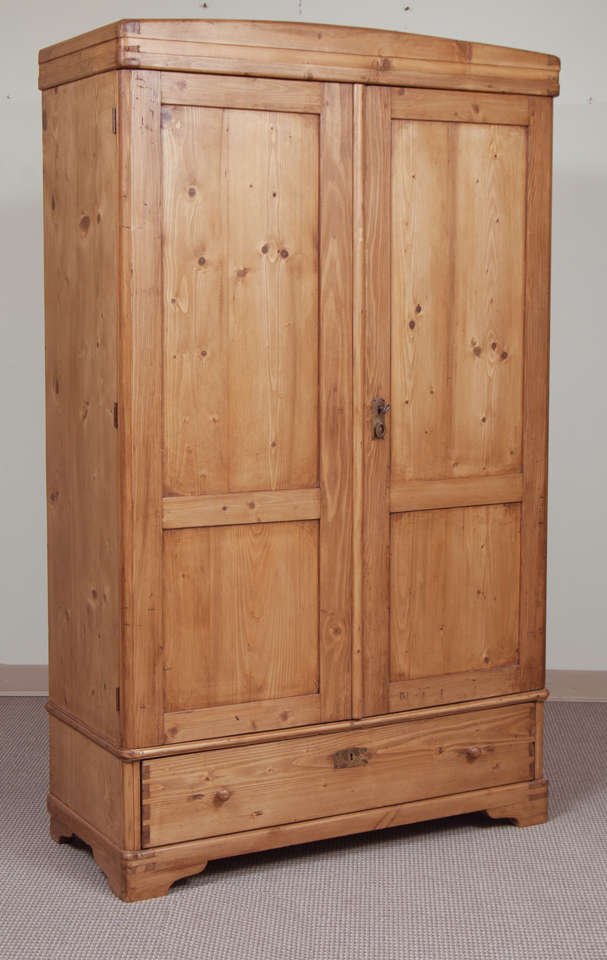 A plain and functional pine armoire, the two panelled doors opening 180 degrees to reveal three replaced shelves above a single hand-cut dovetailed drawer.