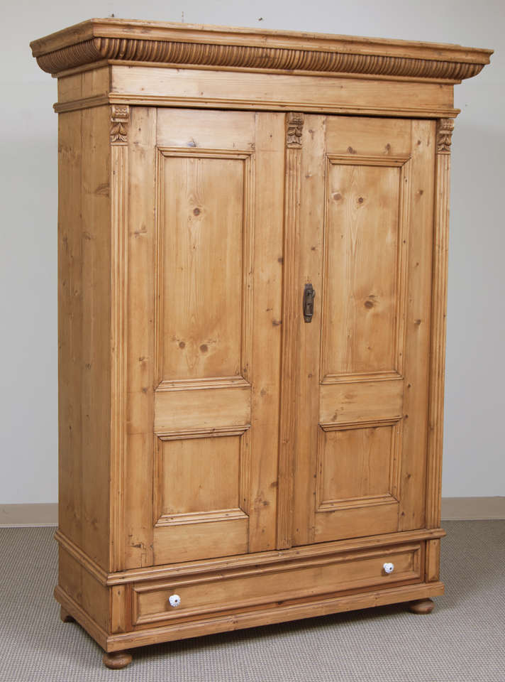 A typically Hungarian two door armoire featuring a boldly decorative crown molding above two panelled doors, flanked and divided by fluted molding and corbels with a single hand-cut dovetailed drawer beneath.  Original ceramic knobs.