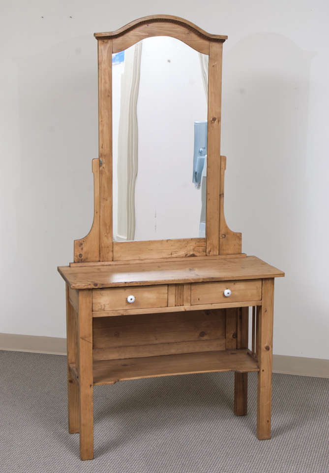 A very attractive dressing table featuring a tall bonnet top mirror with oak egg and dart molding beneath the arch, two hand-cut dovetailed drawers with original ceramic knobs and a shallow scalloped shelf for storage.