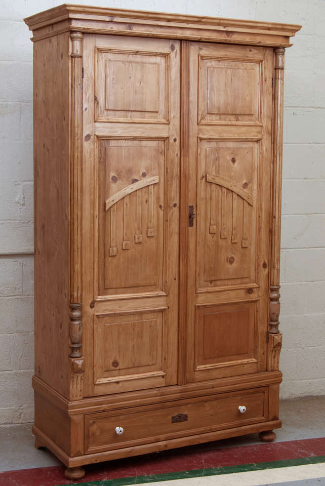 A large pine armoire featuring three raised panels to each door with applied decorative moldings to the centre panel.  The doors are flanked by split balusters with a single hand-cut dovetailed drawer with original ceramic knobs beneath.