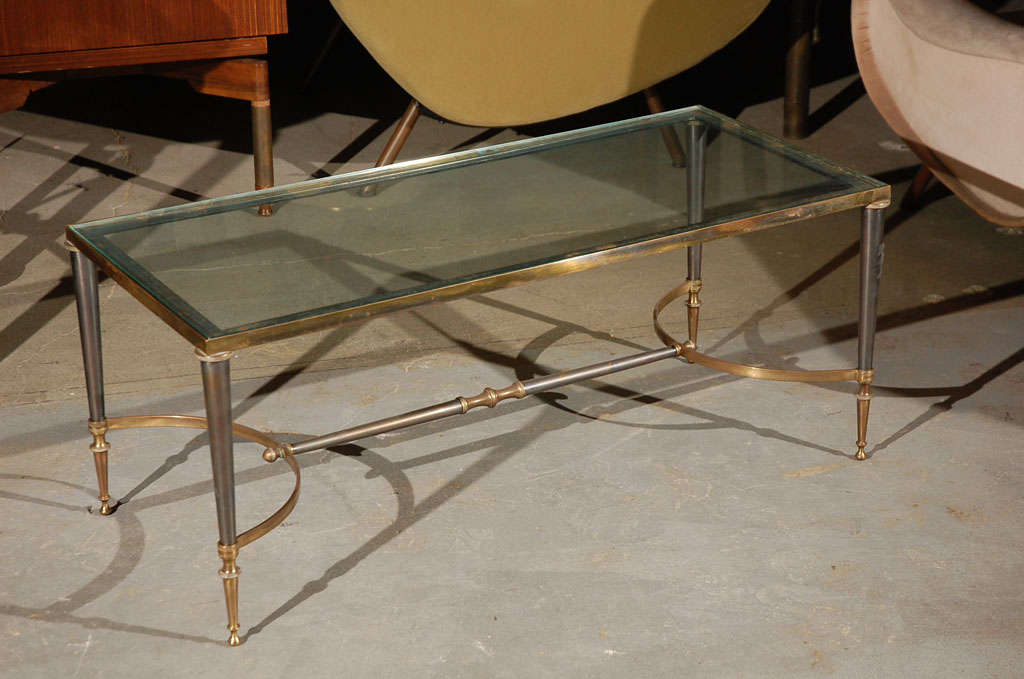 Bronze and steel coffee table with ornate stretcher base and glass top.