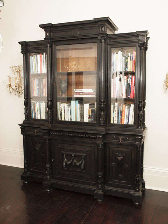Large ebonized breakfront bibliotheque; three glass doors above three cabinets, each flanked with attractively carved pilasters; the lower central door with carved laurel swag; the outer doors with raised panels