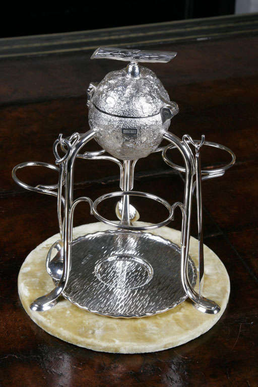 An Arts and Crafts Movement lemon squeezer by Hukin & Heath, the silver plate in the form of a whole lemon with hinged lid, the turnscrew mechanism with a handle in the form of a twig, raised on tall sinuous supports leading to two glass and two