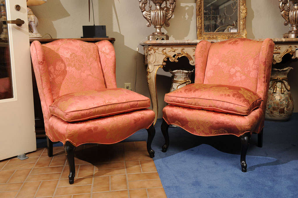 Each with molded wingback over conforming cushion seat above a scalloped seat rail raised on cabriole legs ending on padded feet.  Covered in coral-colored silk damask. In the style of  SYRIE MAUGHAM.