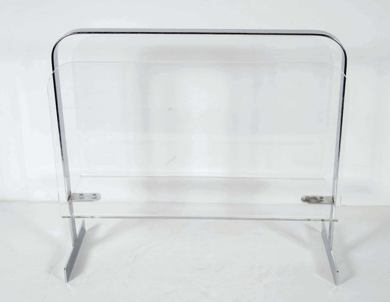This chic magazine stand features a banded chrome T-form support that has Lucite supports. The Lucite has a curved corner detail and a very Art Deco inspiration.