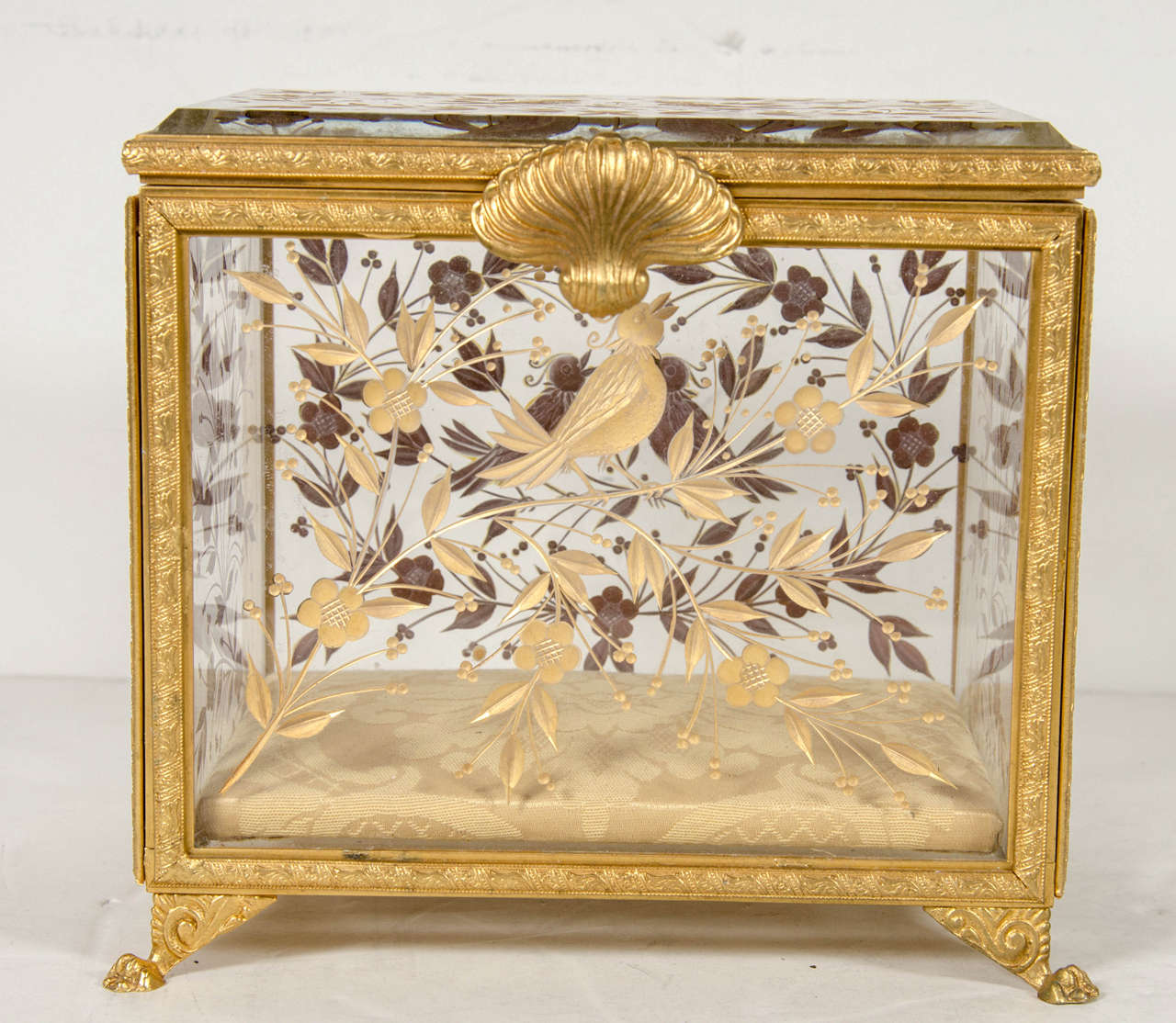 This gorgeous box features an ormolu frame with a stylized shell pull with lions feet and relief detailing throughout . The inset beveled crystal panels feature a stylized flora and fauna design with a bird motif .