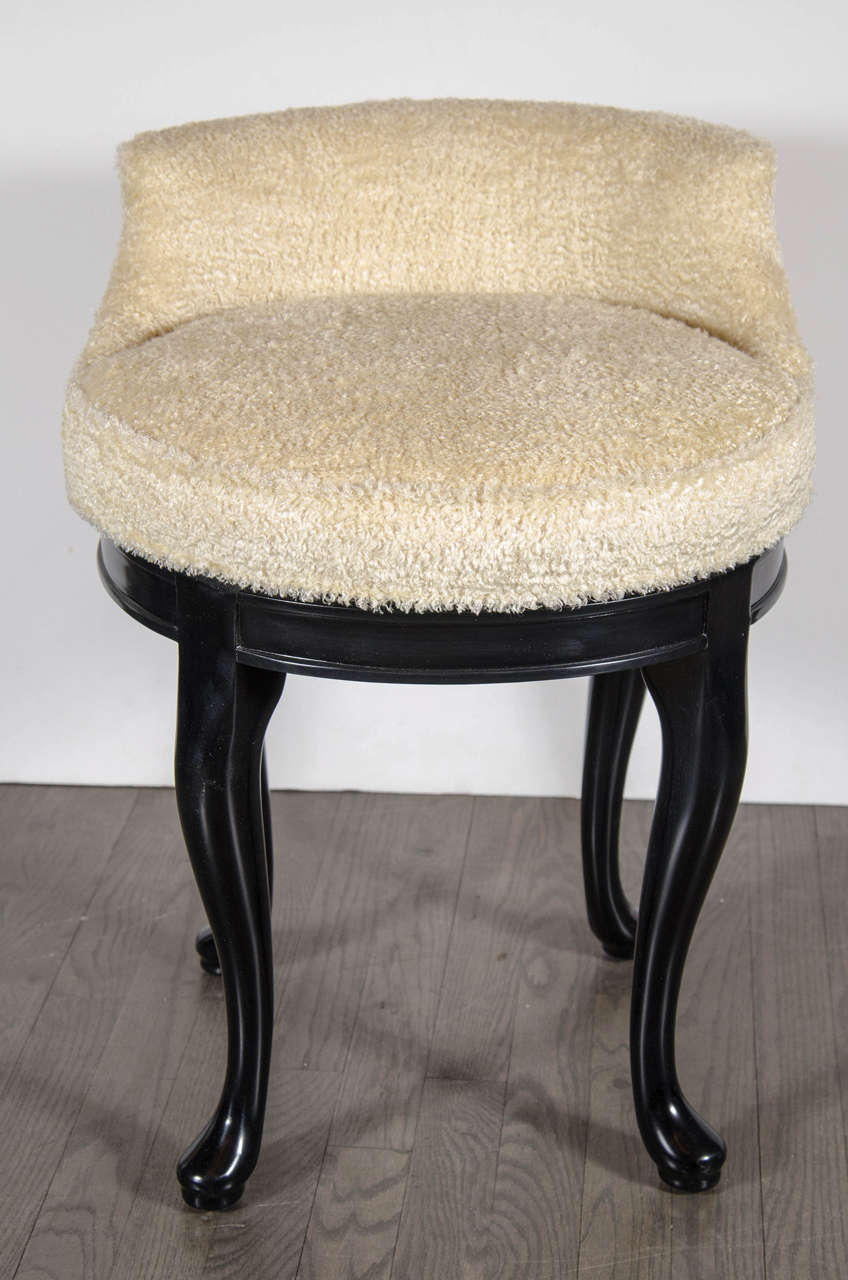 This 1940s Hollywood swivel vanity stool features ebonized walnut cabriole legs, the seat is upholstered in a faux lambs wool and has a low contoured back support. Restored to mint condition.