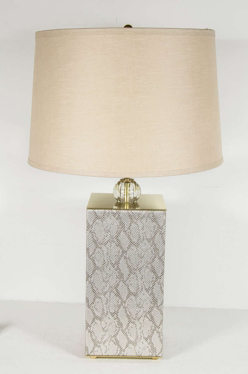 This ultra chic pair of Mid-Century Modernist table lamps feature rectangular bases wrapped in faux python and brass with a glass ball detail at the focal point and brass ball finial. Each lamp accommodates two bulbs which can be used independently