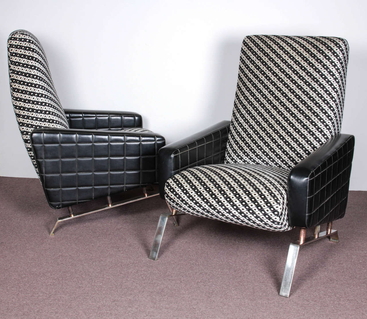 Pair of Italian, wildly stylish tall back lounge chairs of aerodynamic design with original angular nickeled iron bases and original Naugahyde tufted sides. 
The backrest and seats have been newly upholstered in a funky black and white check