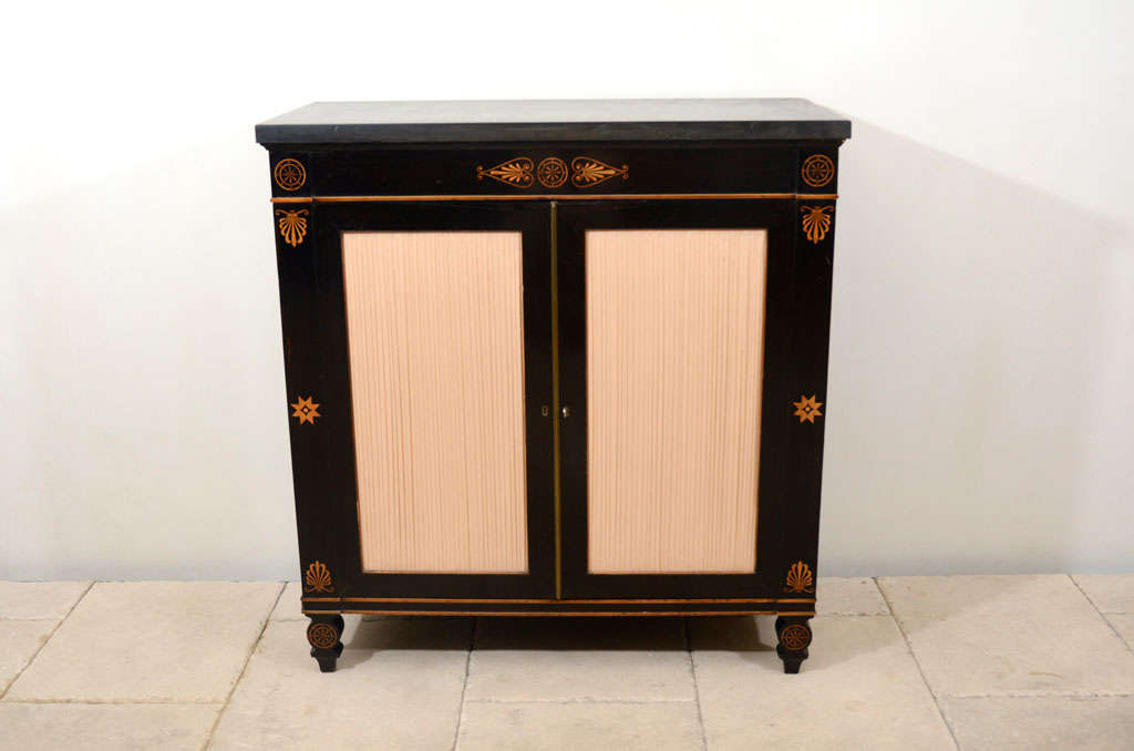 An English Regency ebony and satinwood marquetry inlaid cabinet with double doors opening to interior shelves and a slate top