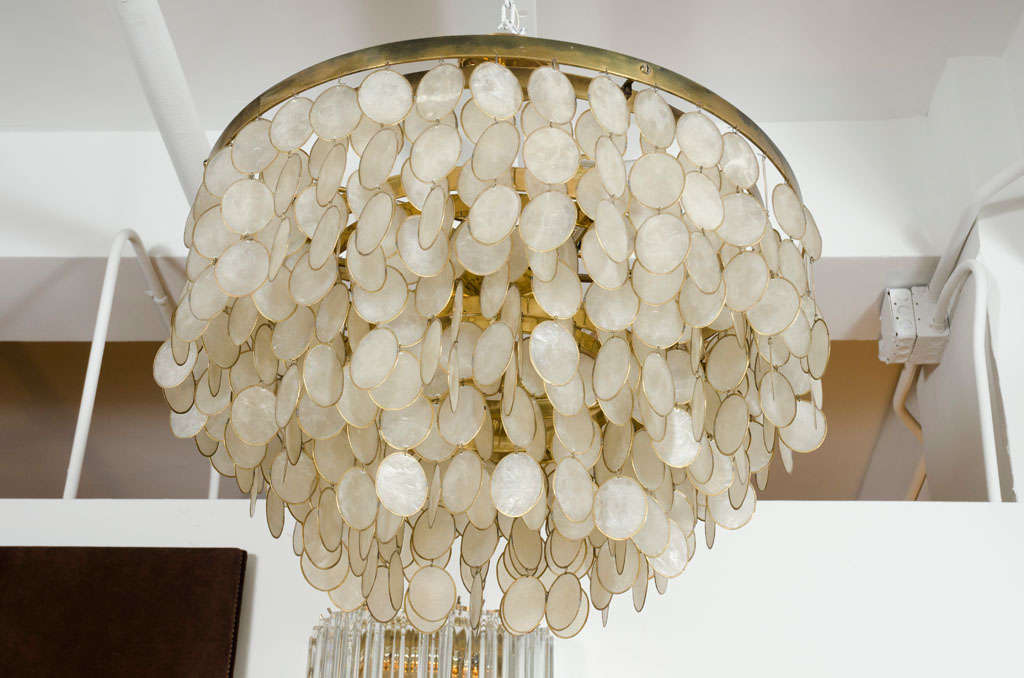 A vintage chandelier comprised of a brass frame with six concentric circles descending in size to form three tiers, each circular frame has dangling links of oval capiz shells set in brass bezels. After Verner Panton. American, circa 1960.