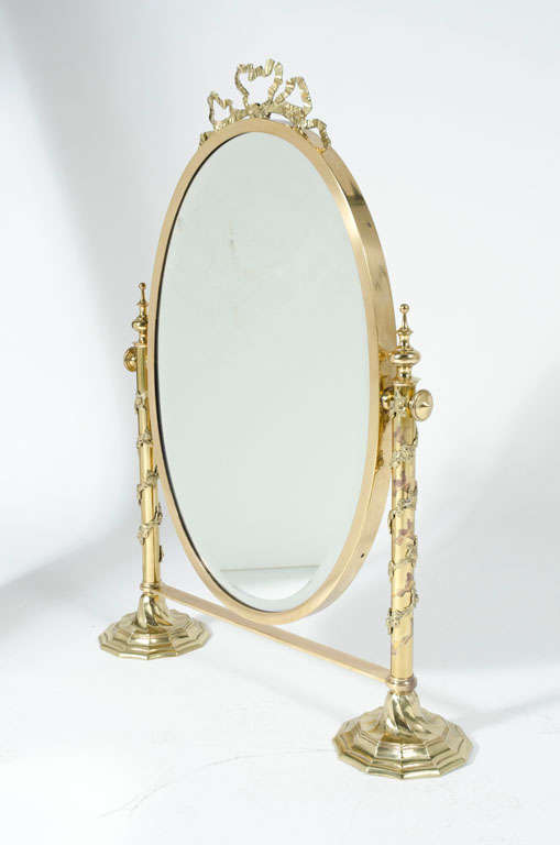 A fantasy tabletop vanity mirror with ribbon crown and garland wrapped posts topped with bishops finials. The oval mirror is set in a brass bezel that tilts and locks into optimal position. Italy, circa 1970.