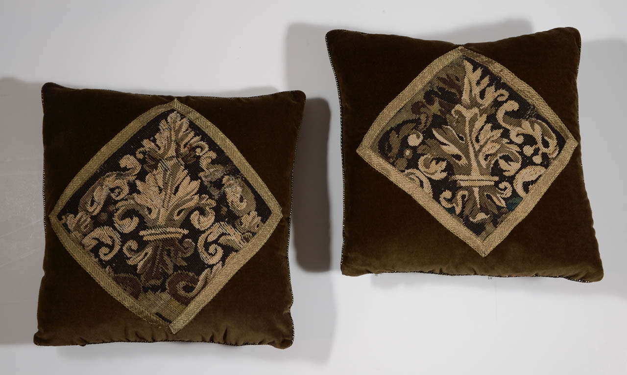 Pair of 18th century tapestry fragment pillows in 100% cotton velvet in rich chocolate hue and finished with gold braid along edge. Tapestries are framed with antique gold ribbon. Down filled.