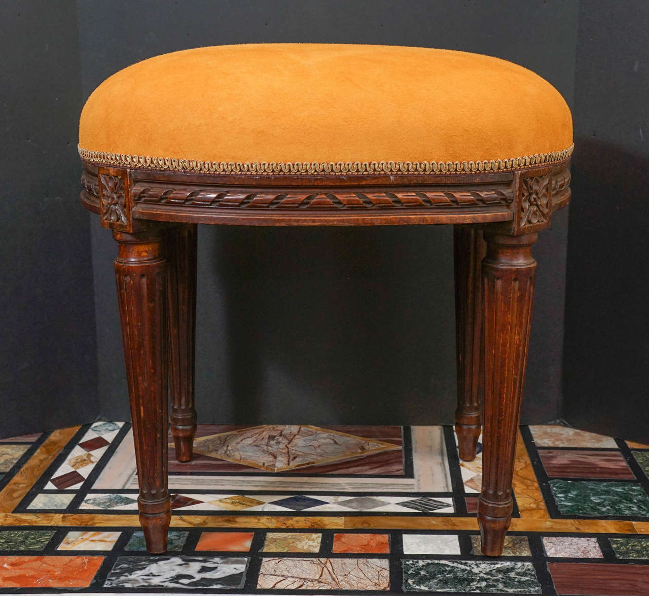 This stool is done in oak with great color and deep rich hand carving. Created in the last decade of the 19th century, the stool's apron is carved in a twisted ribbon that centers on the two long sides but twists in opposite directions from the