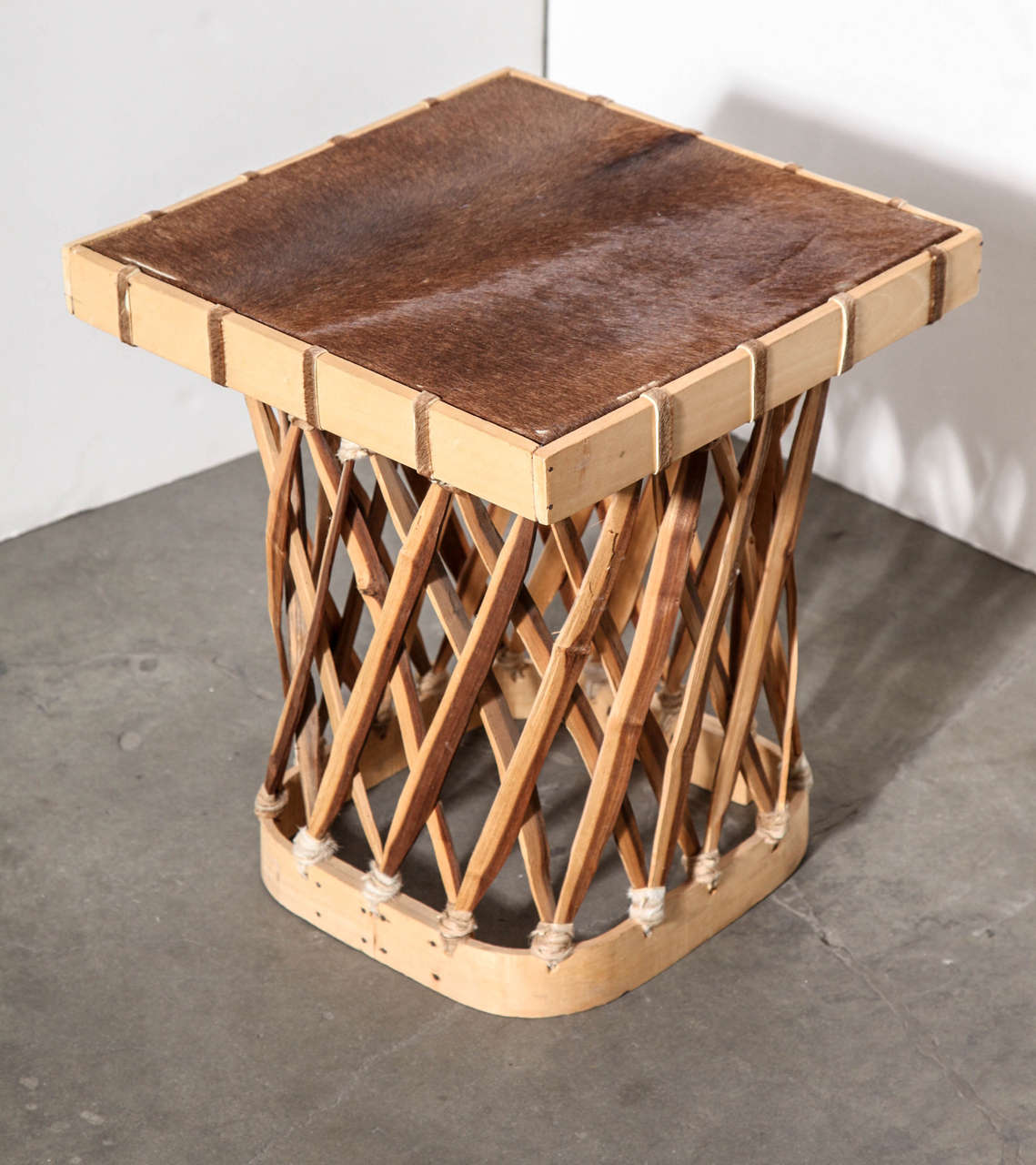 This small wooden table with cowhide top was handcrafted in Mexico. Top is braced underneath with wood. Wood strips along base are secured with leather.