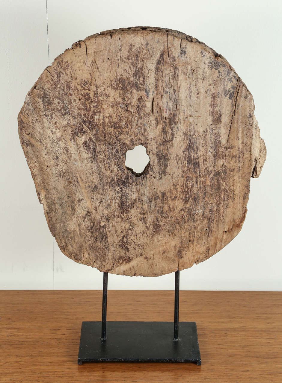 Large reclaimed pierced wooden disc mounted upon a metal display stand.
The wood is worn, with numerous worm holes creating a beautiful textured surface.