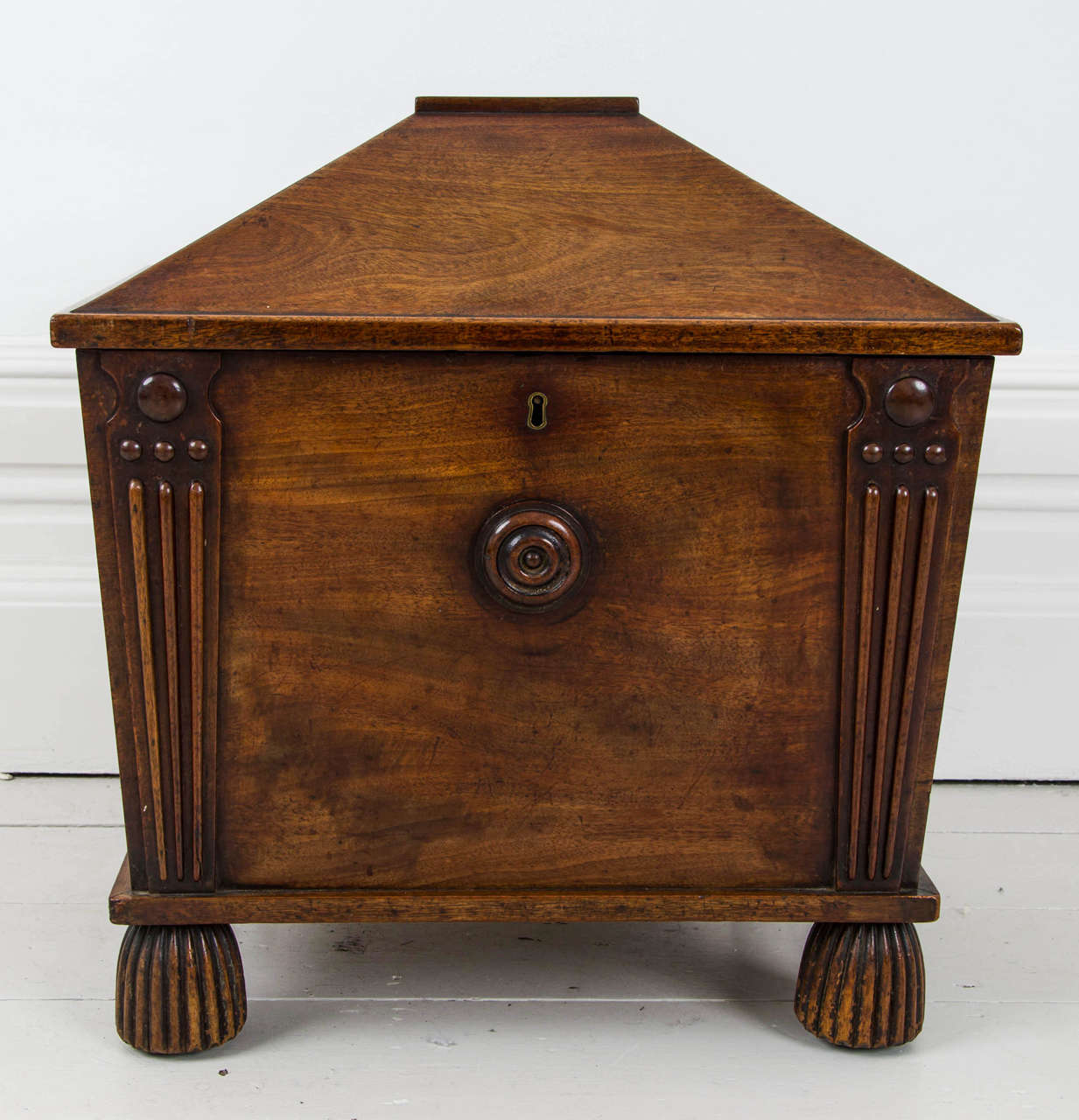 In the manner of Charles Heathcote Tatham. The pitched hinged lid enclosing divisions for bottles, the front with a central moulded roundel and flanked by tapered uprights with roundel decoration, on reeded domed feet with concealed castors.