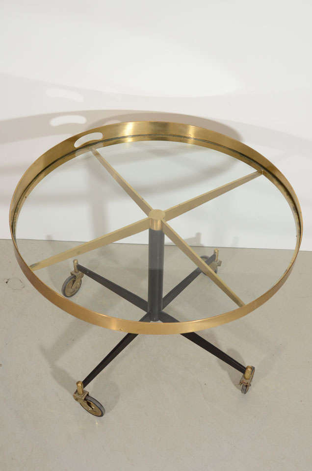 A gently curving, uneven brass rim frames the glass top of this four wheeled cart. This would also make an excellent end table.
