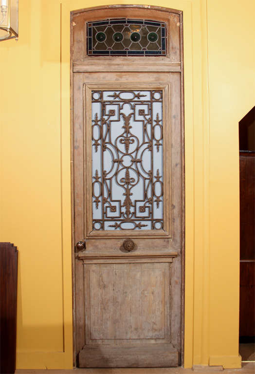 This is a wonderful, early door from Normandy, France.

It features the original transom stained-glass window on the top. This window hinged open for air flow, but has been fixed in place to swing open with the full door.

The center section has