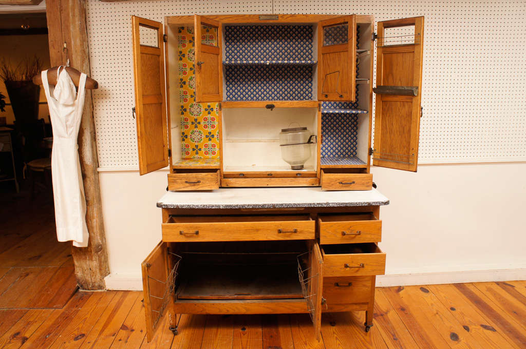 This great Hoosier type kitchen cupboard has all the bells and whistles that one might expect. The upper part has three compartments with shelves and wire racks, the center has a roll door which has an original storage jar attached to one side. It