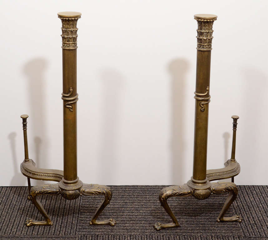 A pair of antique neoclassical andirons in bronze with whimsical footed base supporting a fluted column with snake detail.