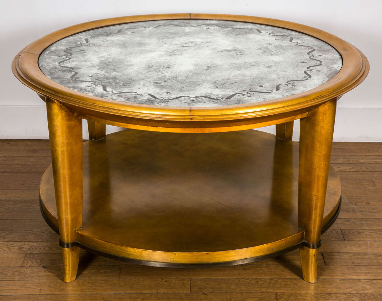 Important gilt lacquered circular wood coffee table, 1938, by A. Arbus (1903-1969) and Max Ingrand (1908-1969).
With gilt lacquered wood structure on four saber feet, together with a bronze belt underneath. Eglomized glass top with engraved