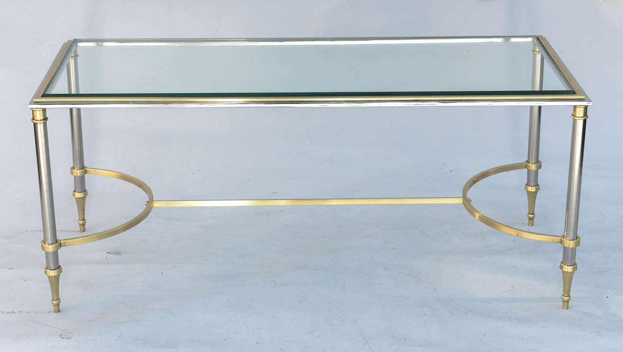 Cocktail table, in the manner of Maison Jansen, having a rectangular top of glass, on base of polished steel with brass accents, raised on round legs, joined by H-stretcher, ending in stylized touipe feet.

Stock ID: D9174